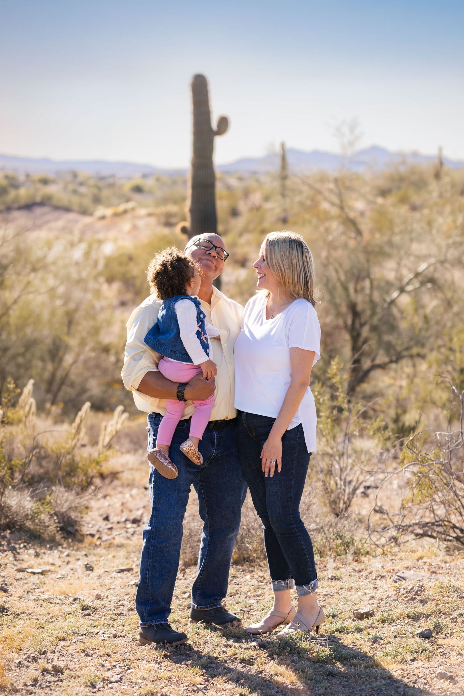 Family of three posing in Arizona desert with saguaro cactus, grandmother holding toddler while smiling at blonde woman.