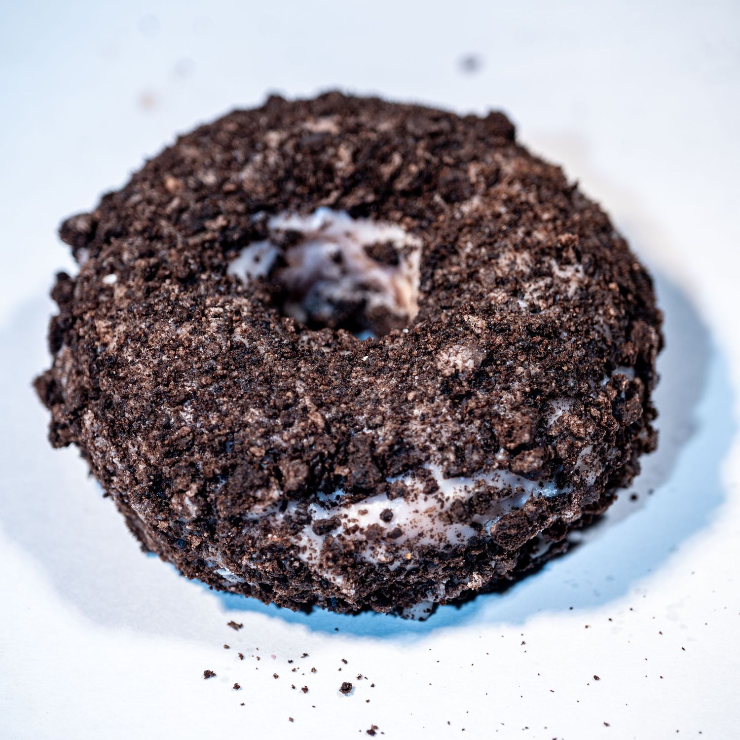 Oreo cookie-covered chocolate donut with cream filling on a white surface.