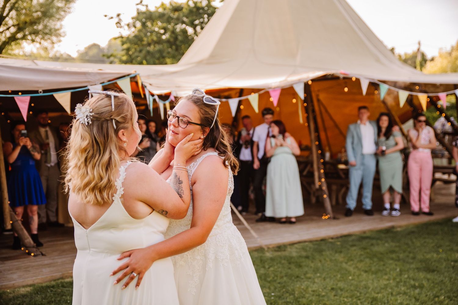 Two brides share an emotional first dance outside a decorated tipi wedding venue with guests watching in the background. The Gaggle of Geese