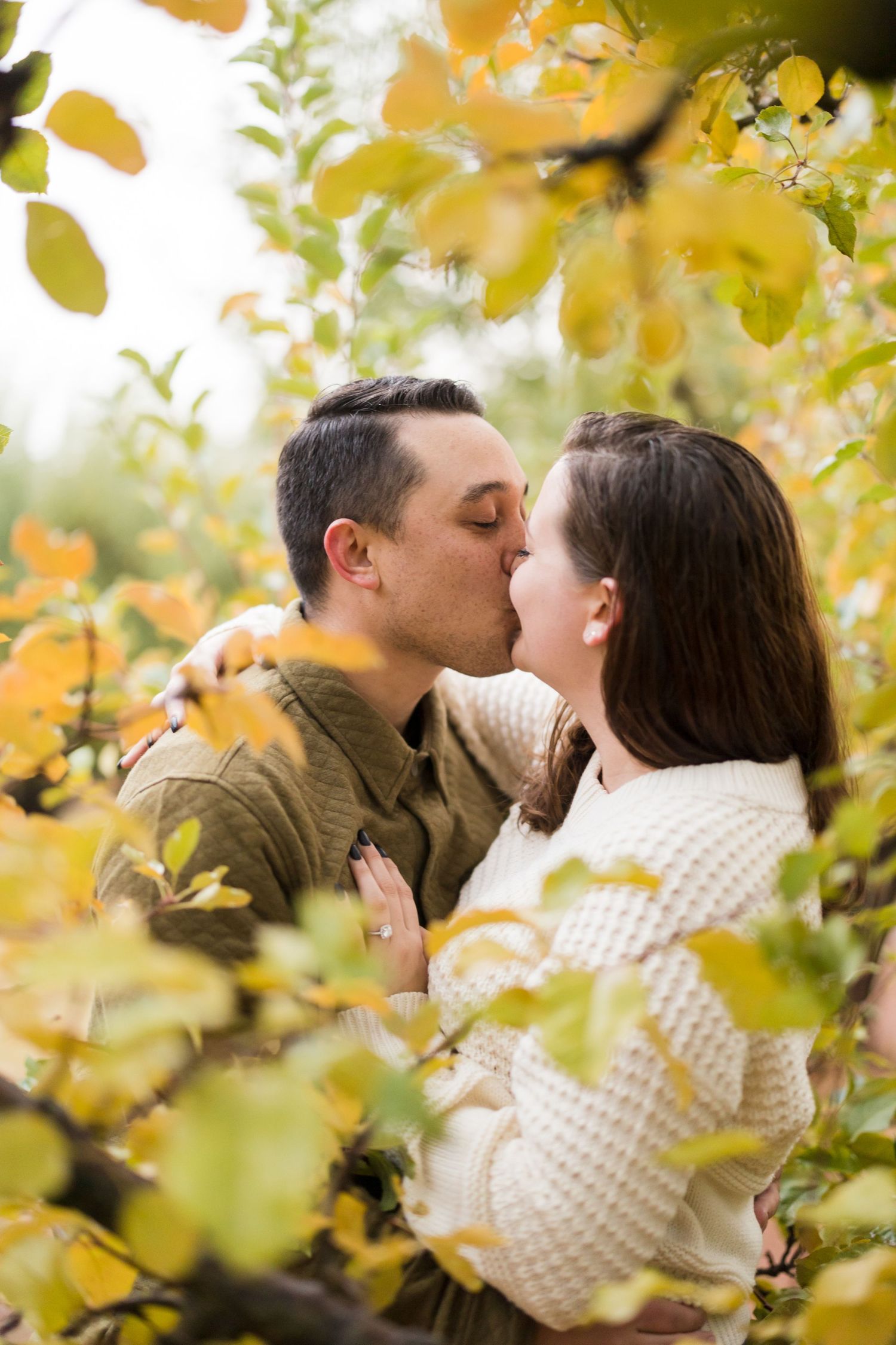 Couple sharing a romantic kiss surrounded by vibrant yellow autumn leaves in an outdoor fall setting.