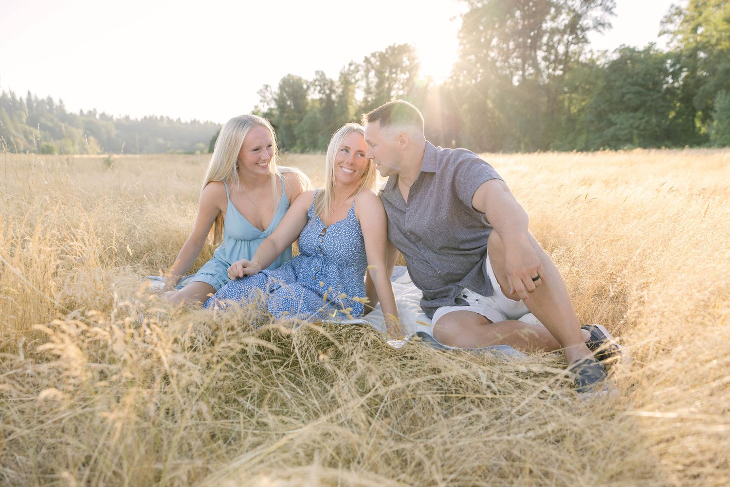Three friends sitting in a golden wheat field during sunset, smiling and enjoying a warm summer day outdoors.