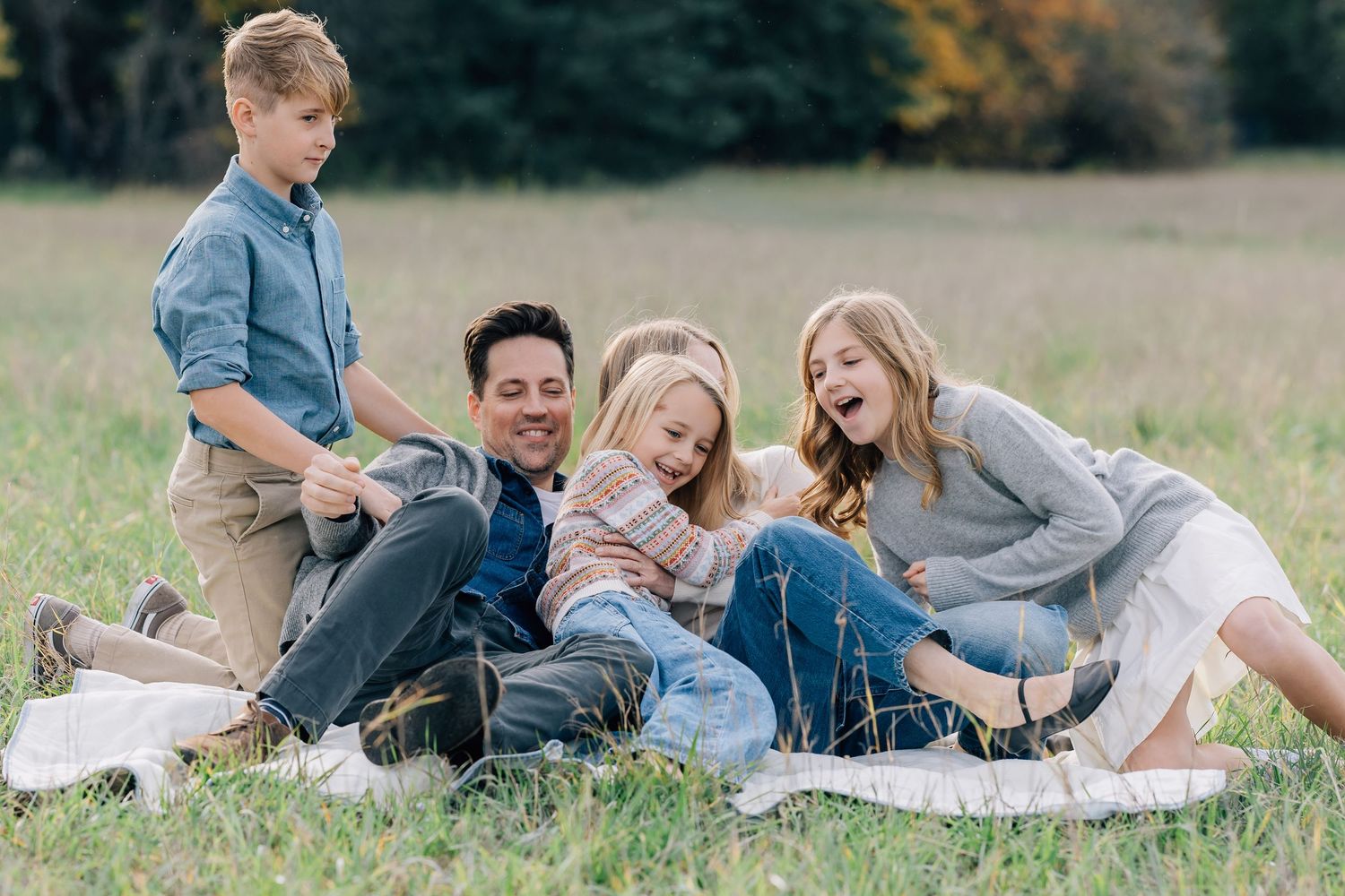 Happy family of four laughing together on a blanket in a green field during a outdoor photo session.