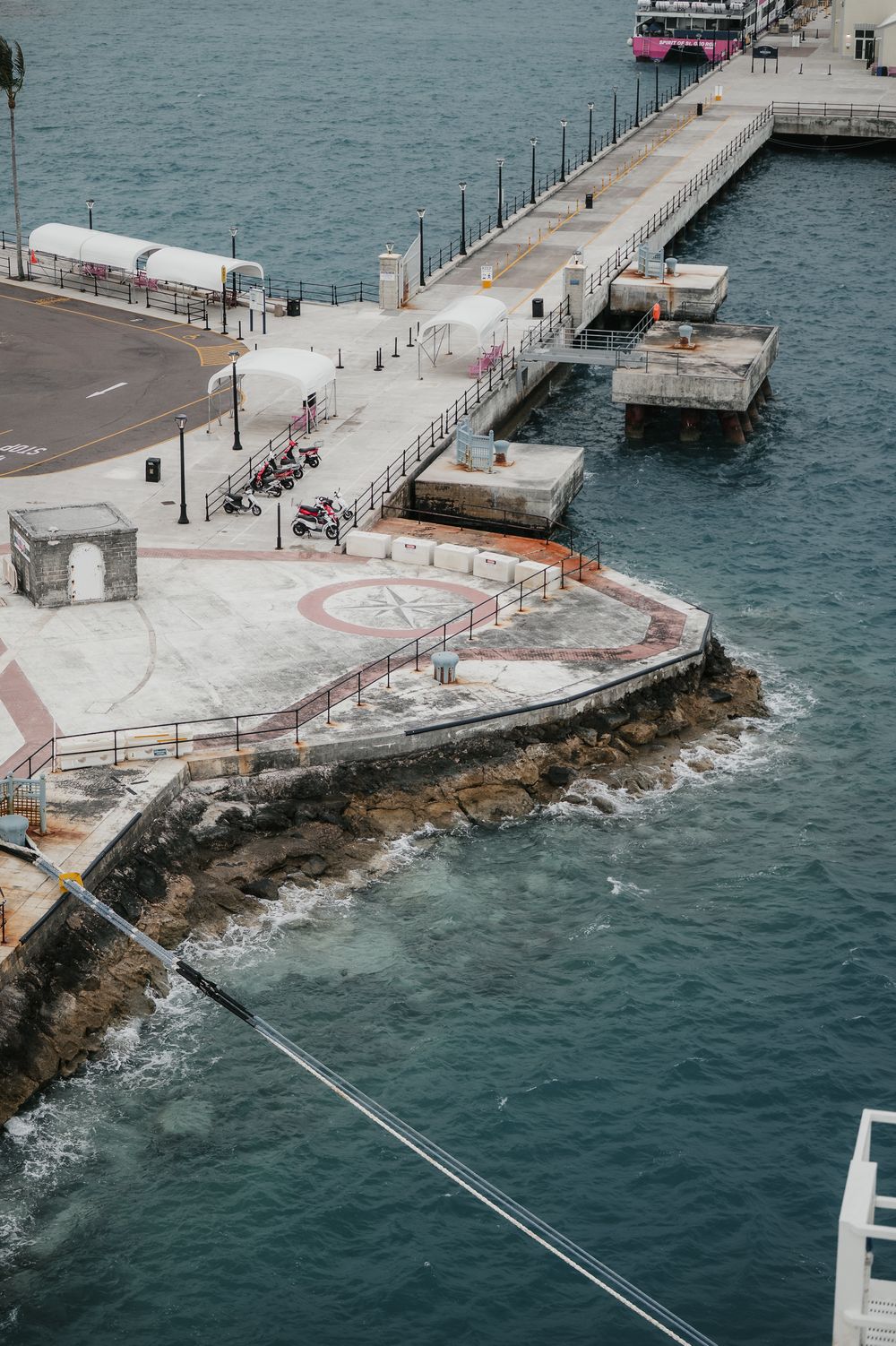Aerial view of a coastal pier with helipad, walkways, and calm blue ocean waters surrounding the concrete dock.