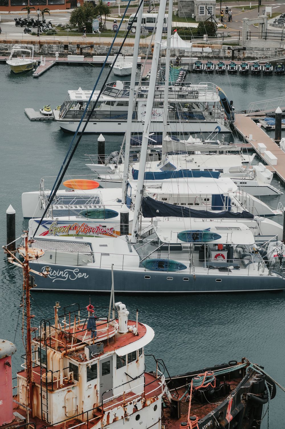 Marina with luxury yachts and sailboats docked alongside a rusty tugboat in a busy harbor.