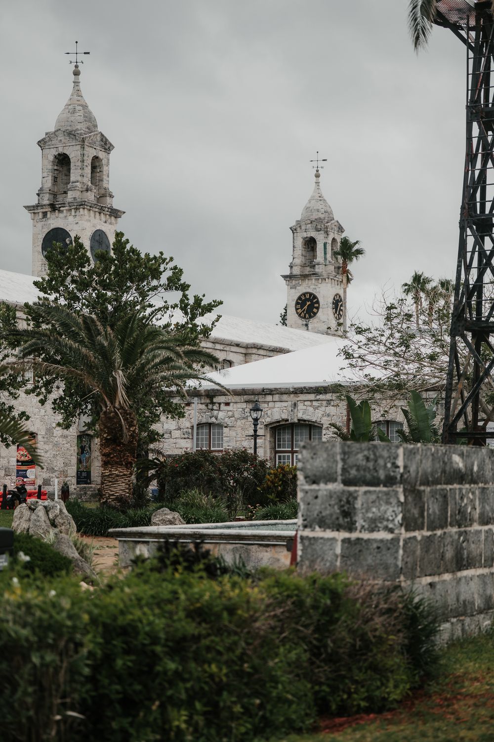 Historic white stone church with twin bell towers surrounded by palm trees and lush greenery under overcast skies.