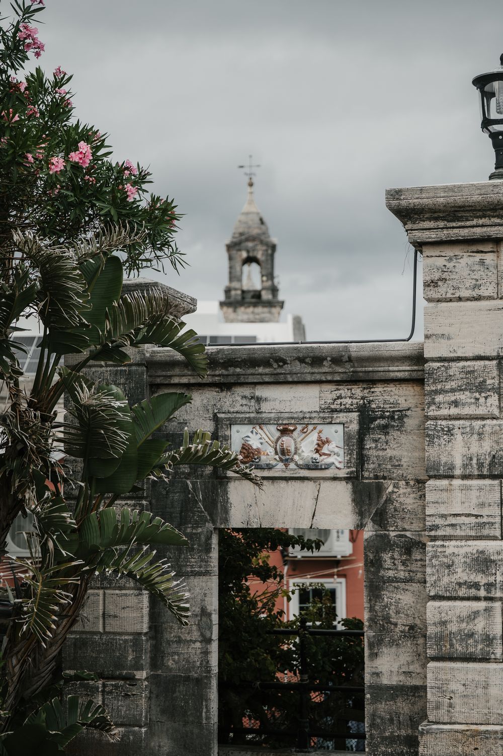 Ancient stone archway gate with decorative crest leading to historic colonial buildings and clock tower in Bermuda.