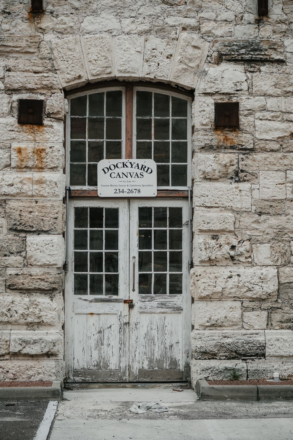 Weathered white wooden doors of historic Dockyard Canvas shop in rustic limestone building in Bermuda.