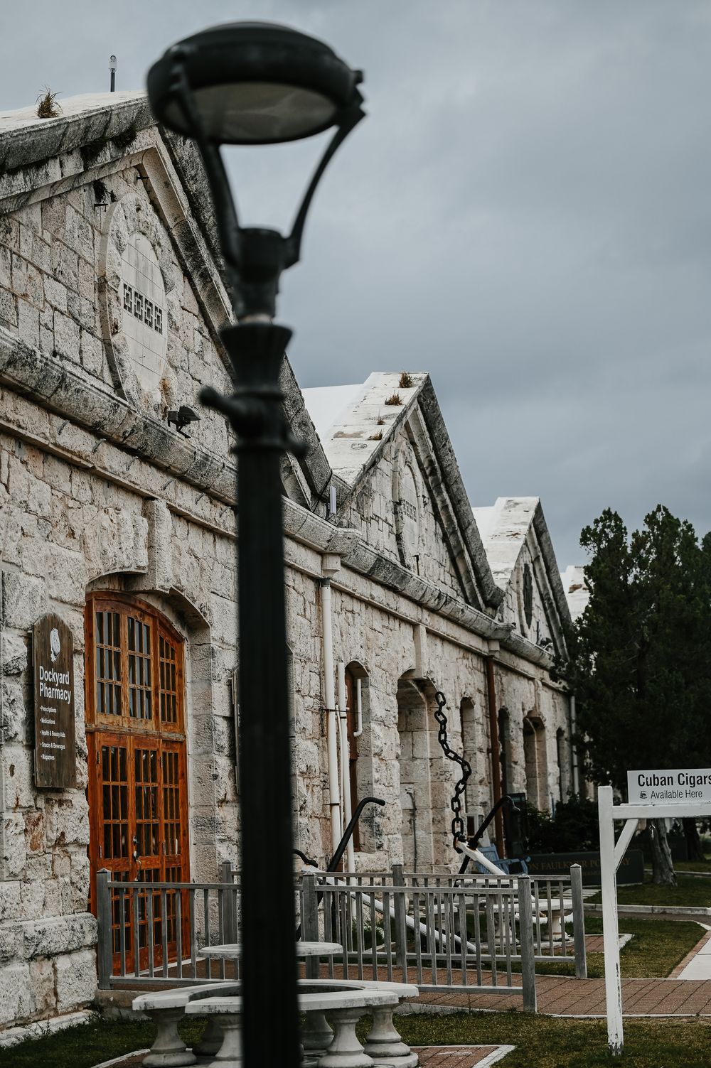 Rustic stone building with orange wooden doors and a black street lamp in the foreground, sign reads Cuban Cigars.