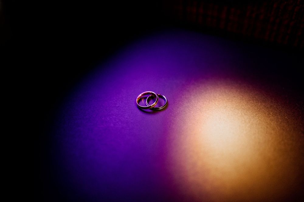 Two gold wedding rings resting on purple and gold illuminated surface in dark setting.