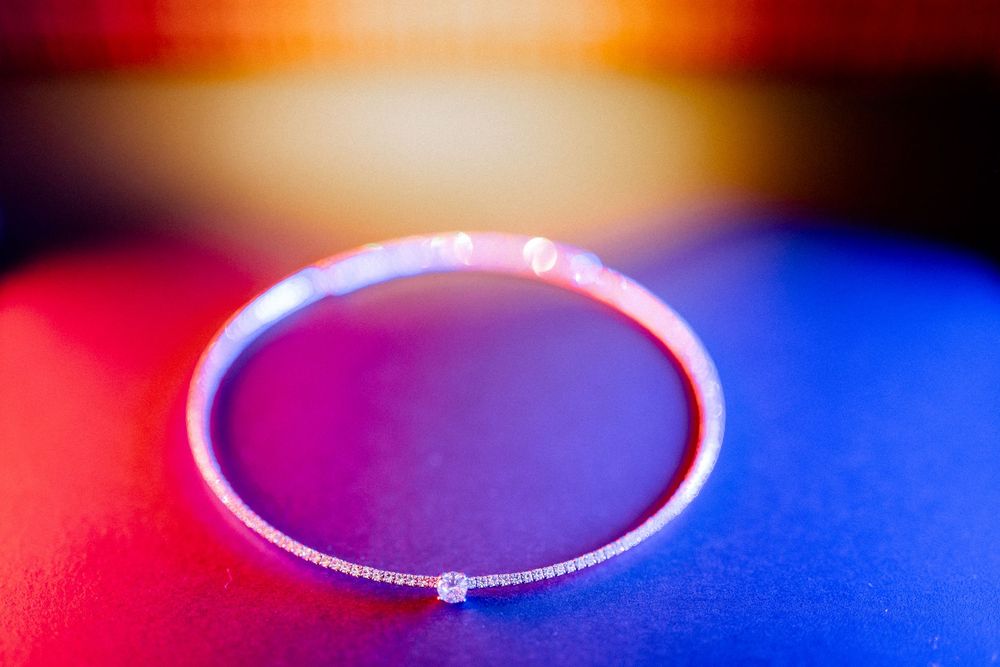 Elegant diamond tennis bracelet on colorful red and blue illuminated background.