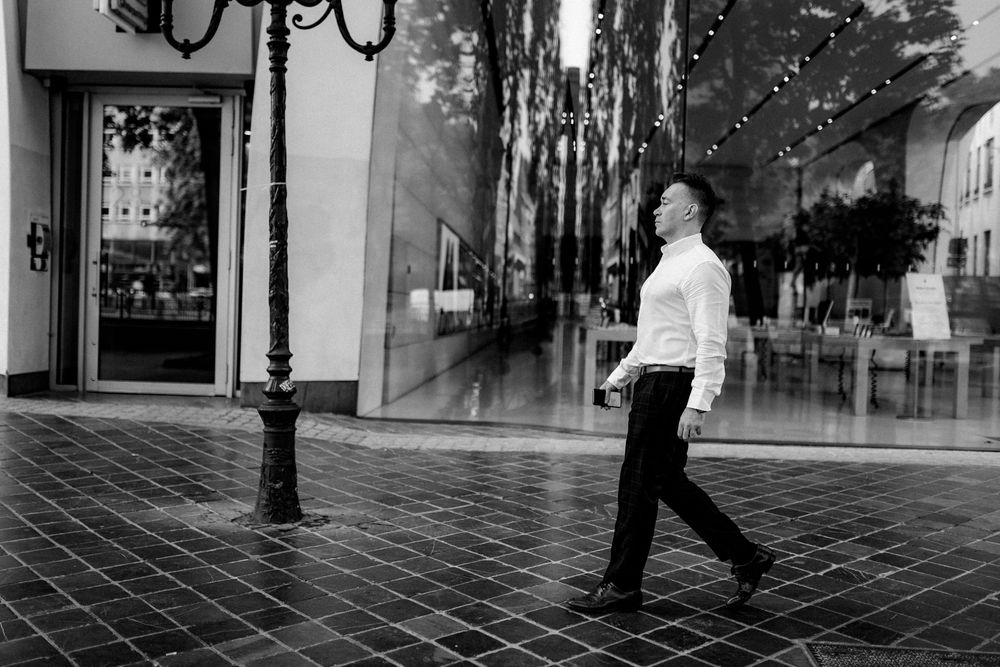 Black and white photo of a man in white shirt and black pants walking past a large reflective storefront window.