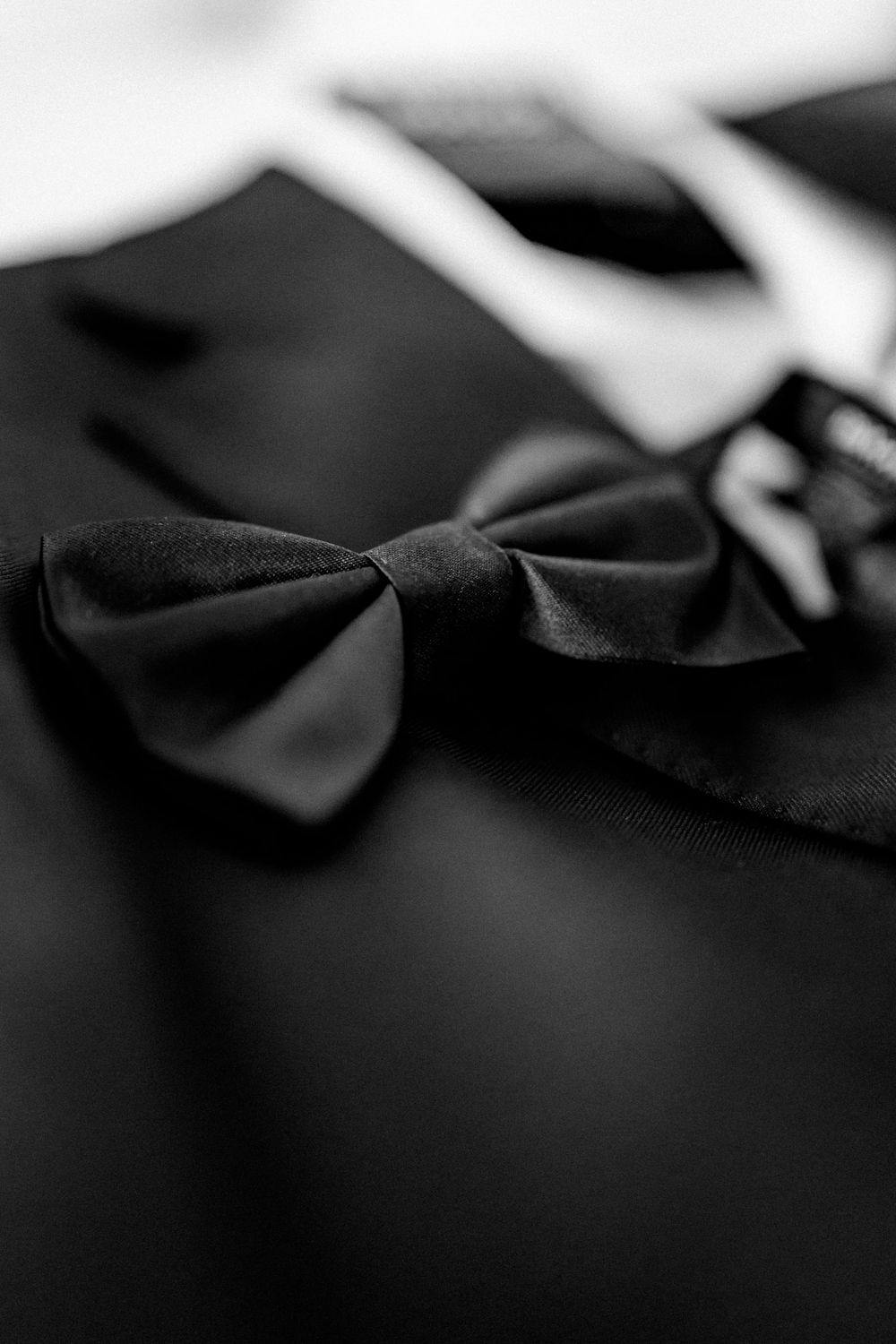 Close-up black and white photo of a classic black bow tie on a formal tuxedo jacket.