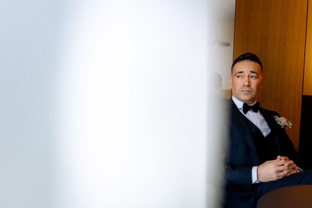 Dapper groom in a navy tuxedo with bow tie and boutonniere sits thoughtfully before the wedding ceremony.