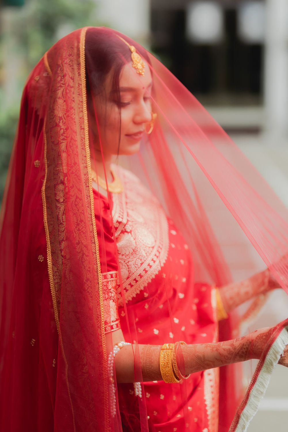 Indian bride in red bridal lehenga with gold jewelry and dupatta veil, eyes closed in serene pose.