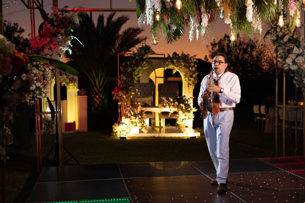 Musician playing saxophone at an elegant outdoor wedding reception with floral decorations and warm lighting.