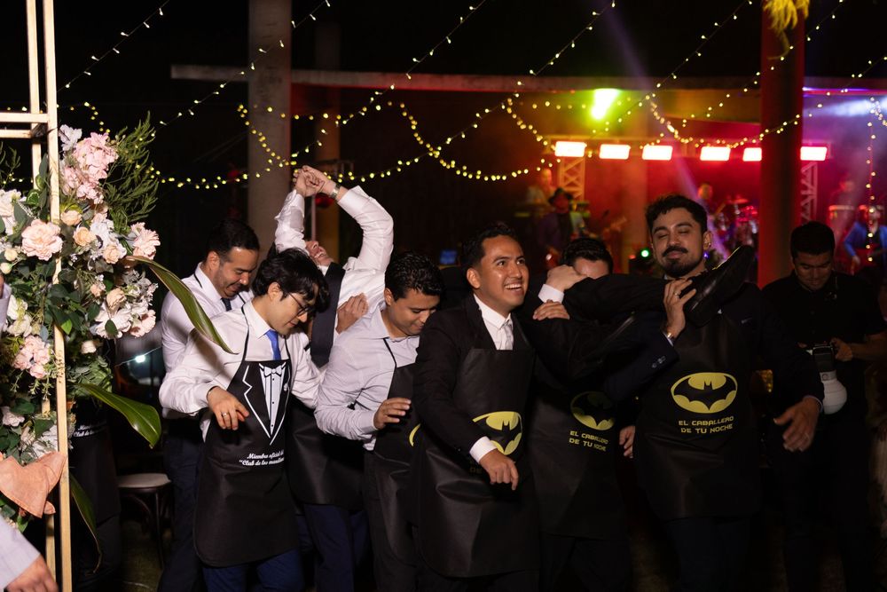 Group of men in suits dancing and celebrating at an outdoor evening wedding reception party.