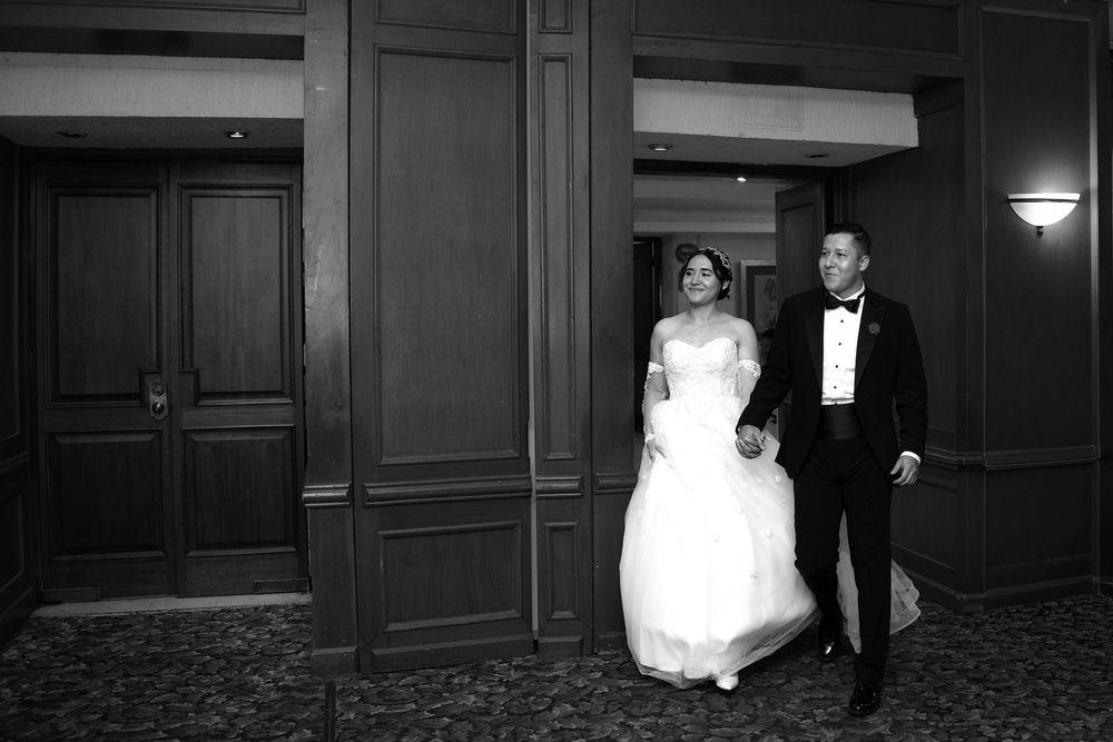 Black and white photo of a bride and groom walking hand in hand through an elegant hotel corridor.