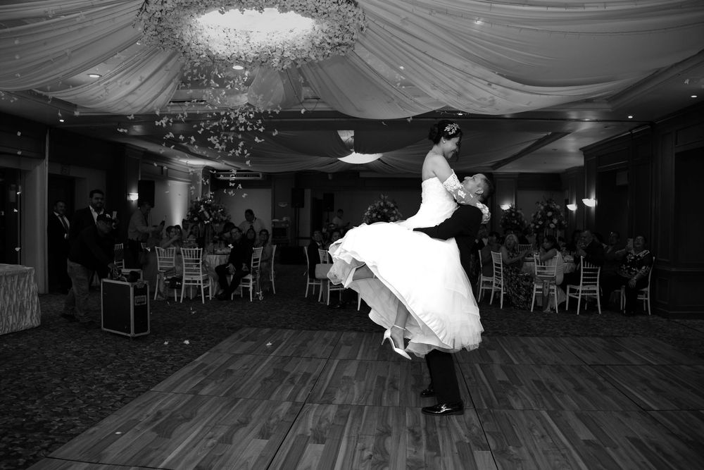 Black and white photo of groom lifting bride during first dance at elegant wedding reception ballroom.