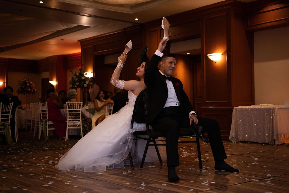 Bride and groom playfully raise their shoes during a wedding reception game in an elegant ballroom.