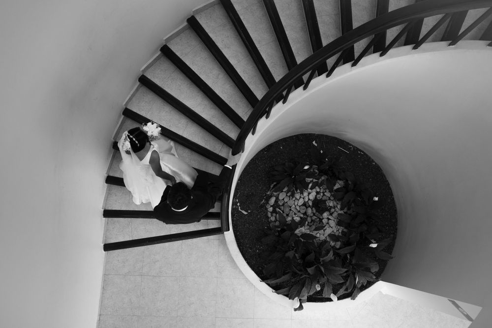 Black and white aerial view of a couple in wedding attire on a spiral staircase.