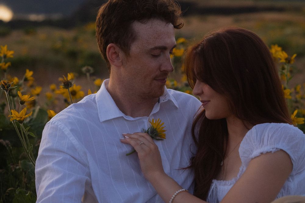 Couple sharing a romantic moment in a sunflower field at golden hour, woman placing flower on mans chest.