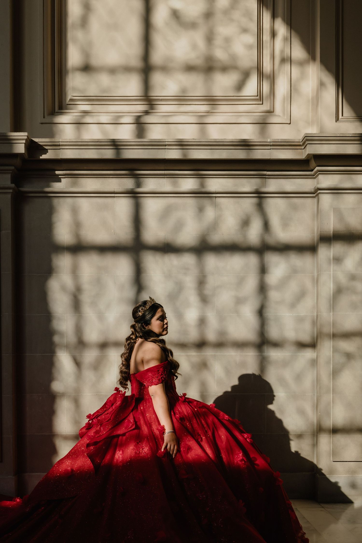 Woman in blue ball gown poses by a pond in front of a white castle-like mansion on a sunny day.