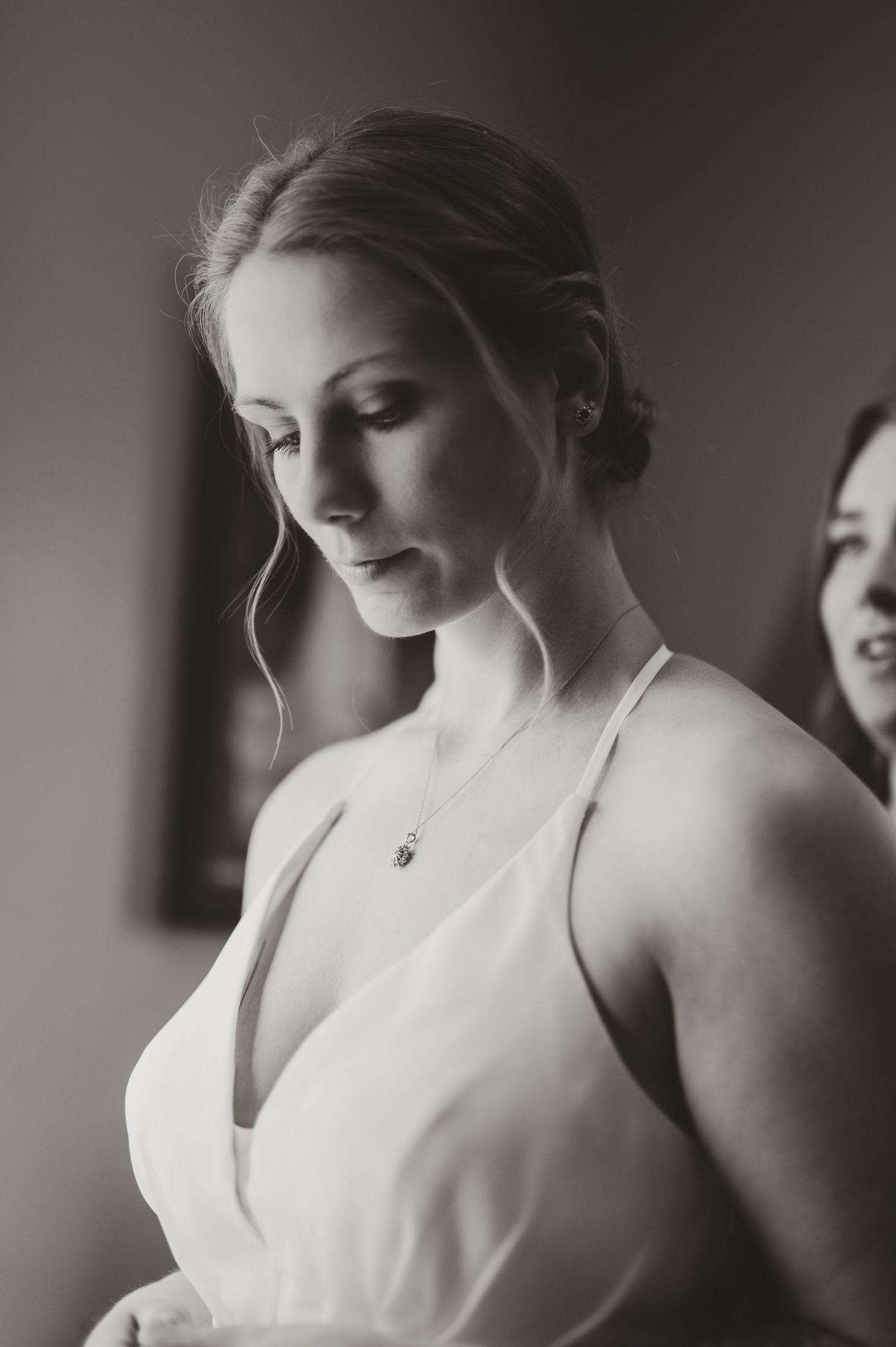 Black and white photo of a bride in a white gown with a delicate necklace, looking down before her wedding in Southeast Wisconsin