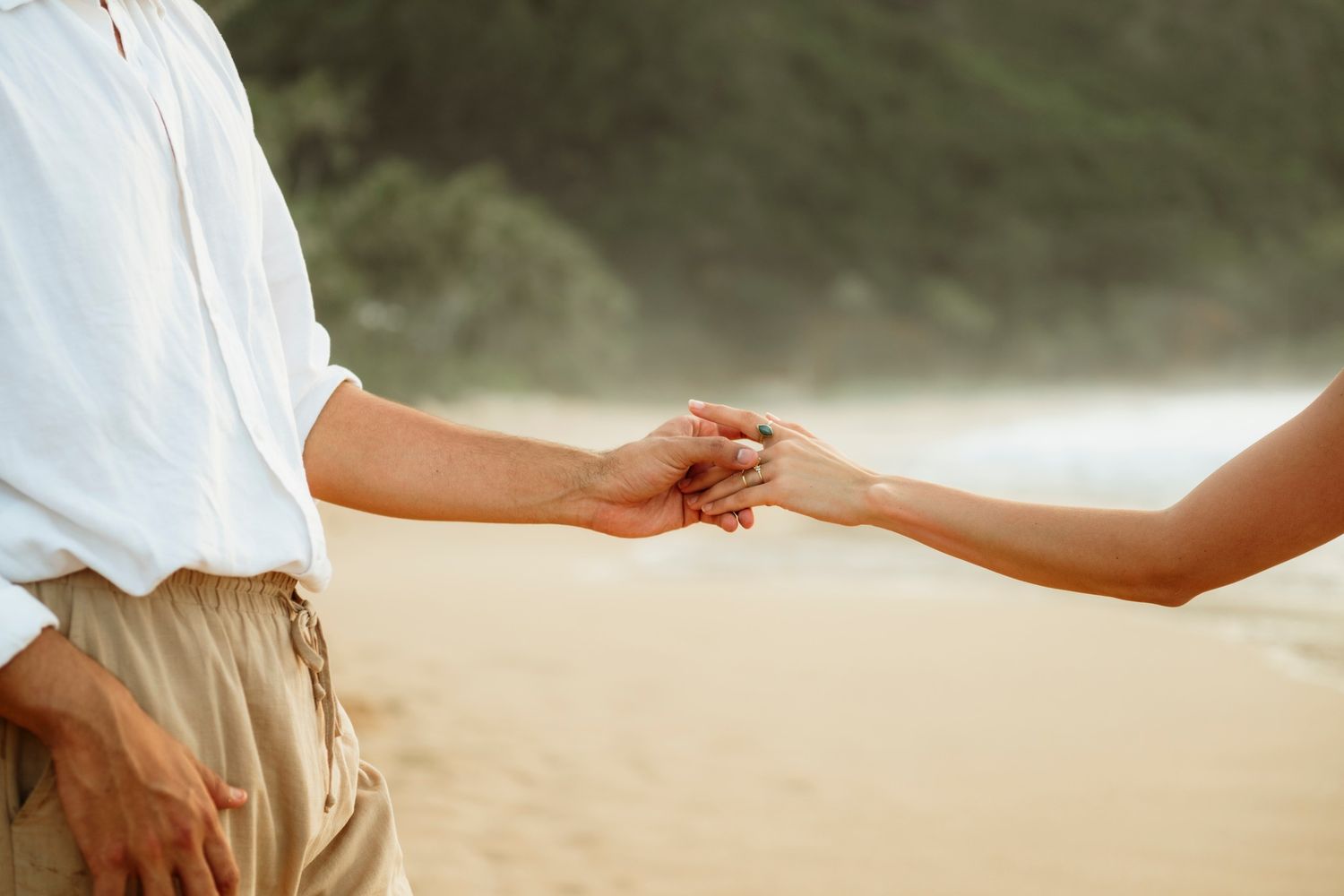 Couple holding hands tenderly on a sandy beach with soft misty background.