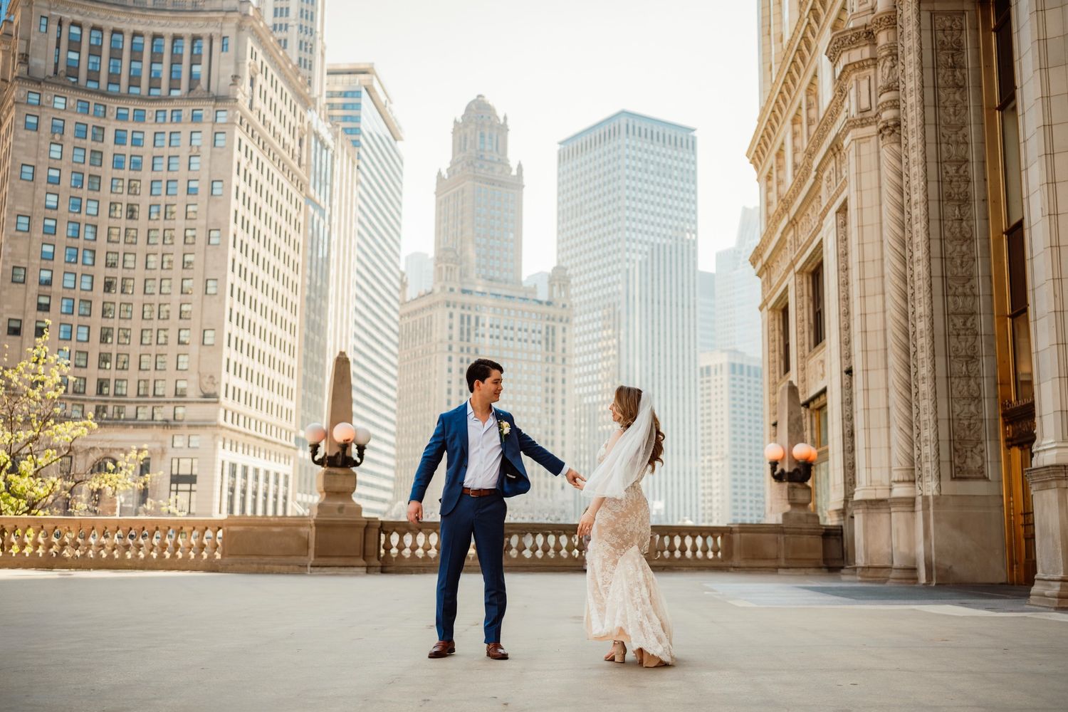 Couple holds hands dancing in Chicago city plaza surrounded by stunning skyscrapers on a sunny day.