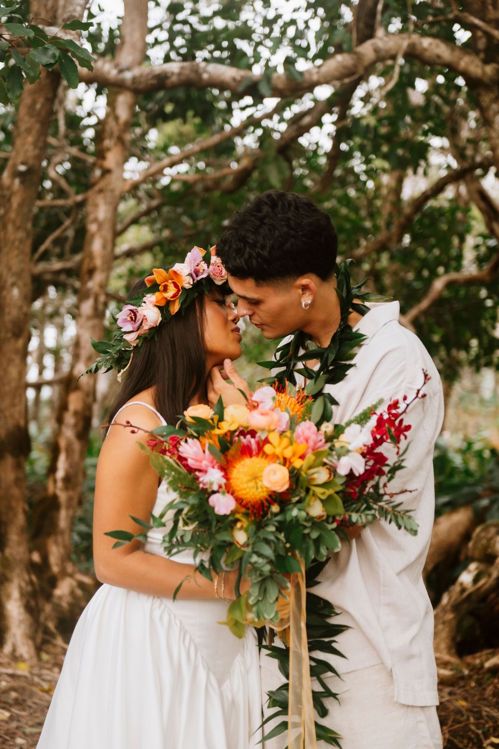 Couple sharing a romantic moment in a tropical garden, bride wearing floral crown holding vibrant bouquet.