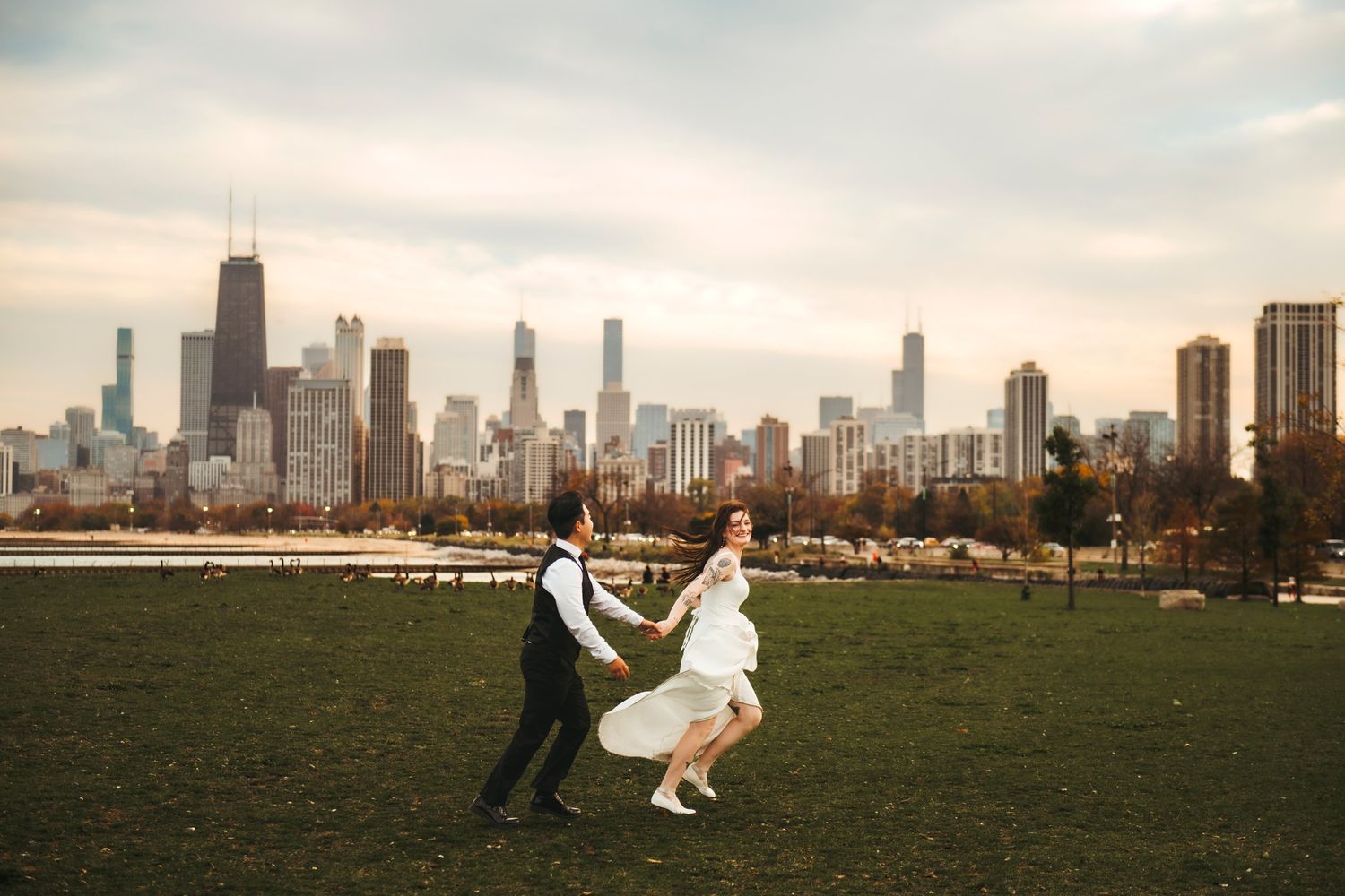 Bride and groom dancing on green lawn with Chicago skyline backdrop on cloudy day.