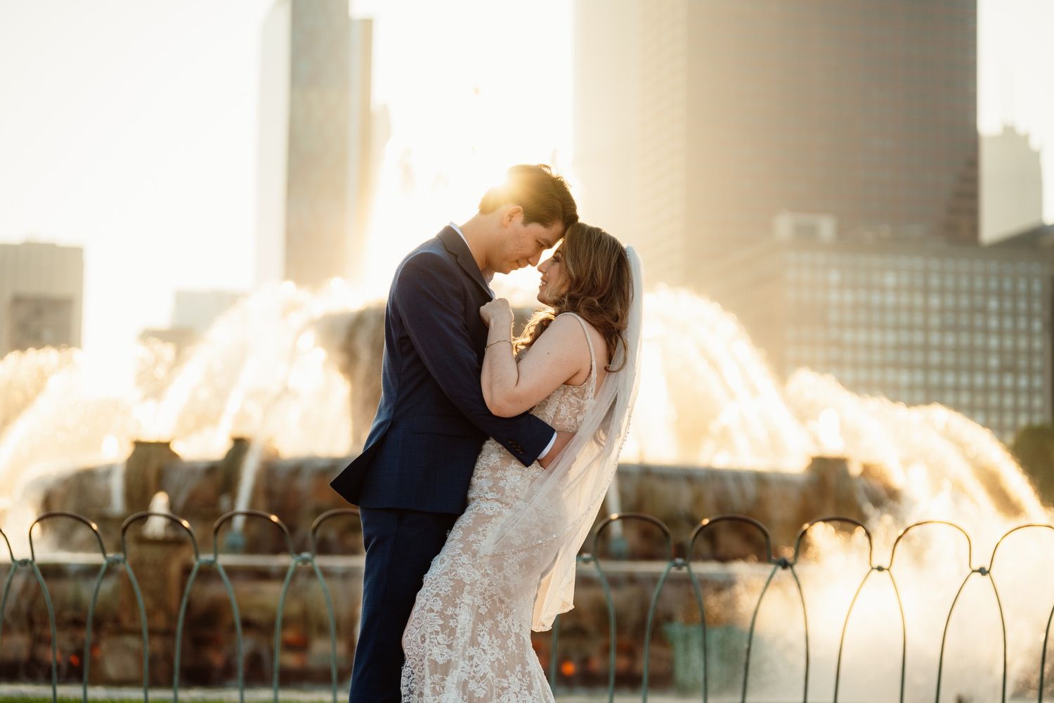 Couple sharing romantic kiss in front of glowing Buckingham Fountain at golden hour.