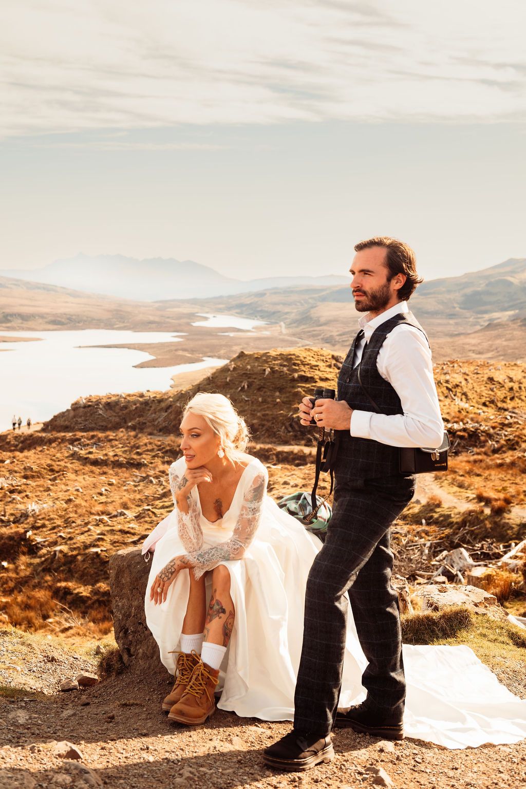 Wedding couple posing on rugged highland terrain with scenic lake and mountains behind them.