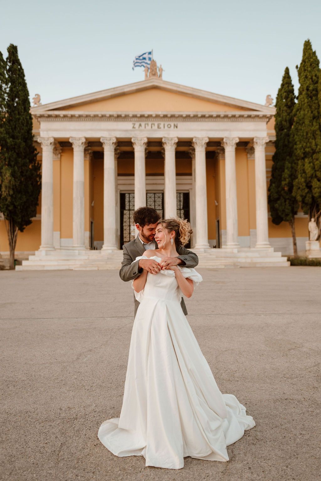 Wedding couple embracing in front of the neoclassical Zappeion building in Athens, Greece.