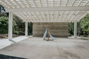 Modern pergola with white lattice roof over concrete patio featuring a sculptural sailboat artwork against a stone wall.