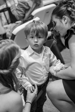 Black and white photo of a young boy in white shirt between two women at a formal event.