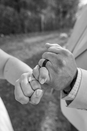 Black and white photo of a couple holding hands, showing wedding and engagement rings, symbolizing love and commitment.