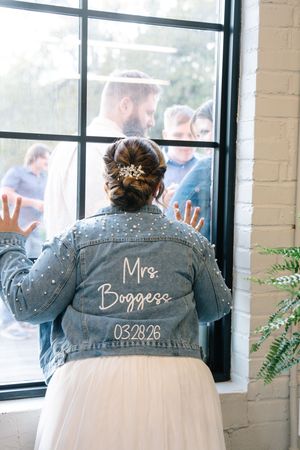 Bride wearing a pearl-embellished denim jacket customized with Mrs. Boggess and wedding date 03.28.26.