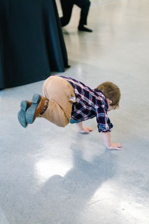 Young boy in plaid shirt and tan pants doing a handstand on a shiny indoor floor.