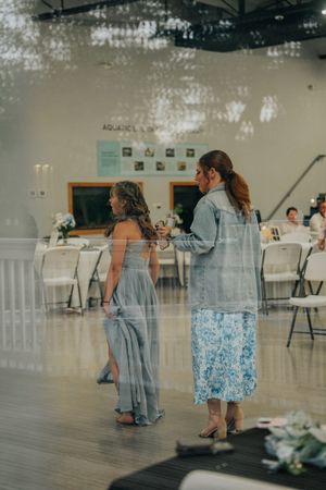 Two women in elegant attire stand on a dance floor at a wedding reception venue.