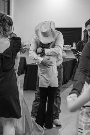 Black and white photo of couple embracing on dance floor, man wearing cowboy hat at indoor event.