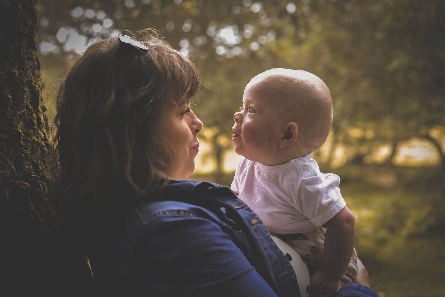 A sweet moment of bonding between adult and baby outdoors during golden hour with sunlight filtering through trees.