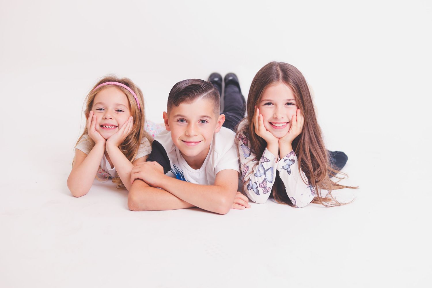Siblings laying on white floor in studio for family portrait.
