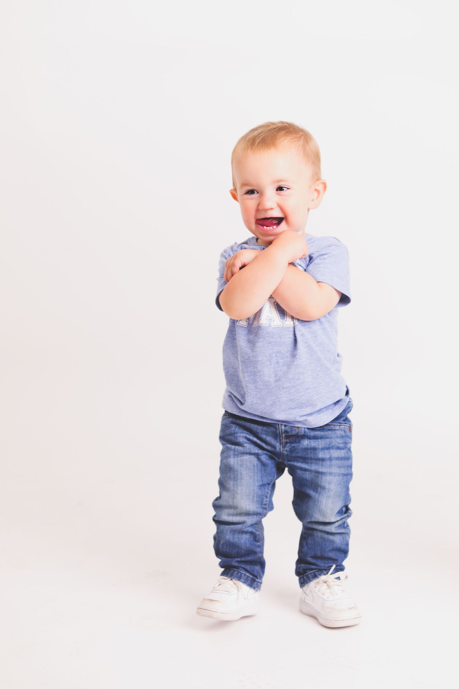 Happy toddler in gray shirt and jeans against white background.
