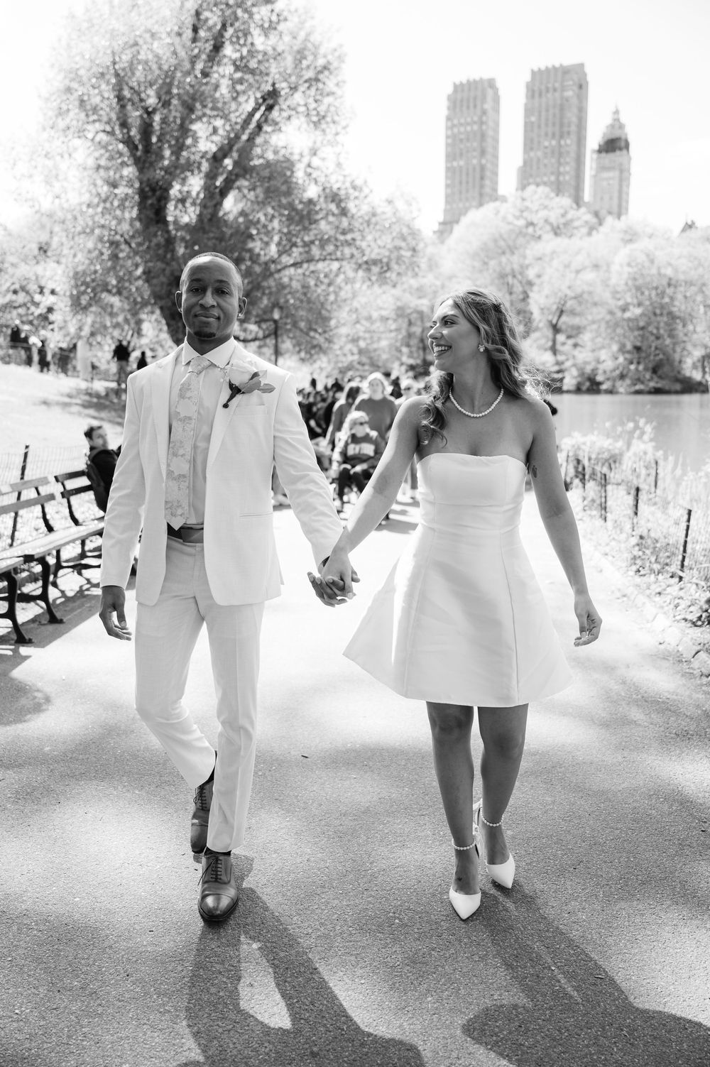 Black and white photo of newlyweds holding hands walking through Central Park after ceremony.