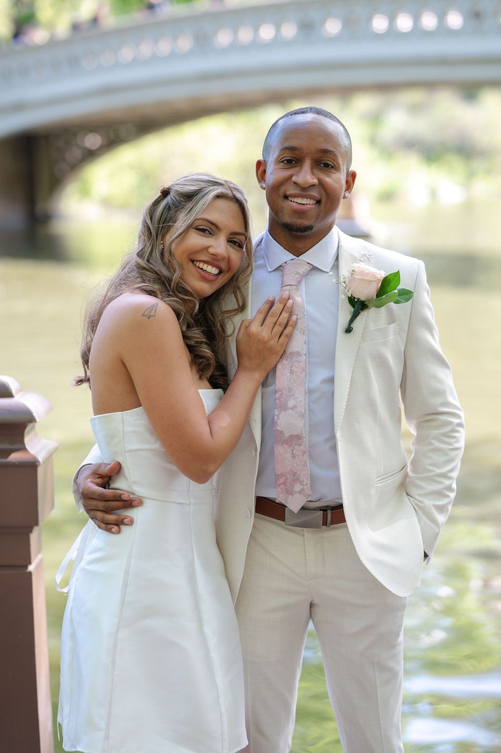 A newlywed couple smiles together near Bow Bridge in Central Park, NYC, on their wedding day.