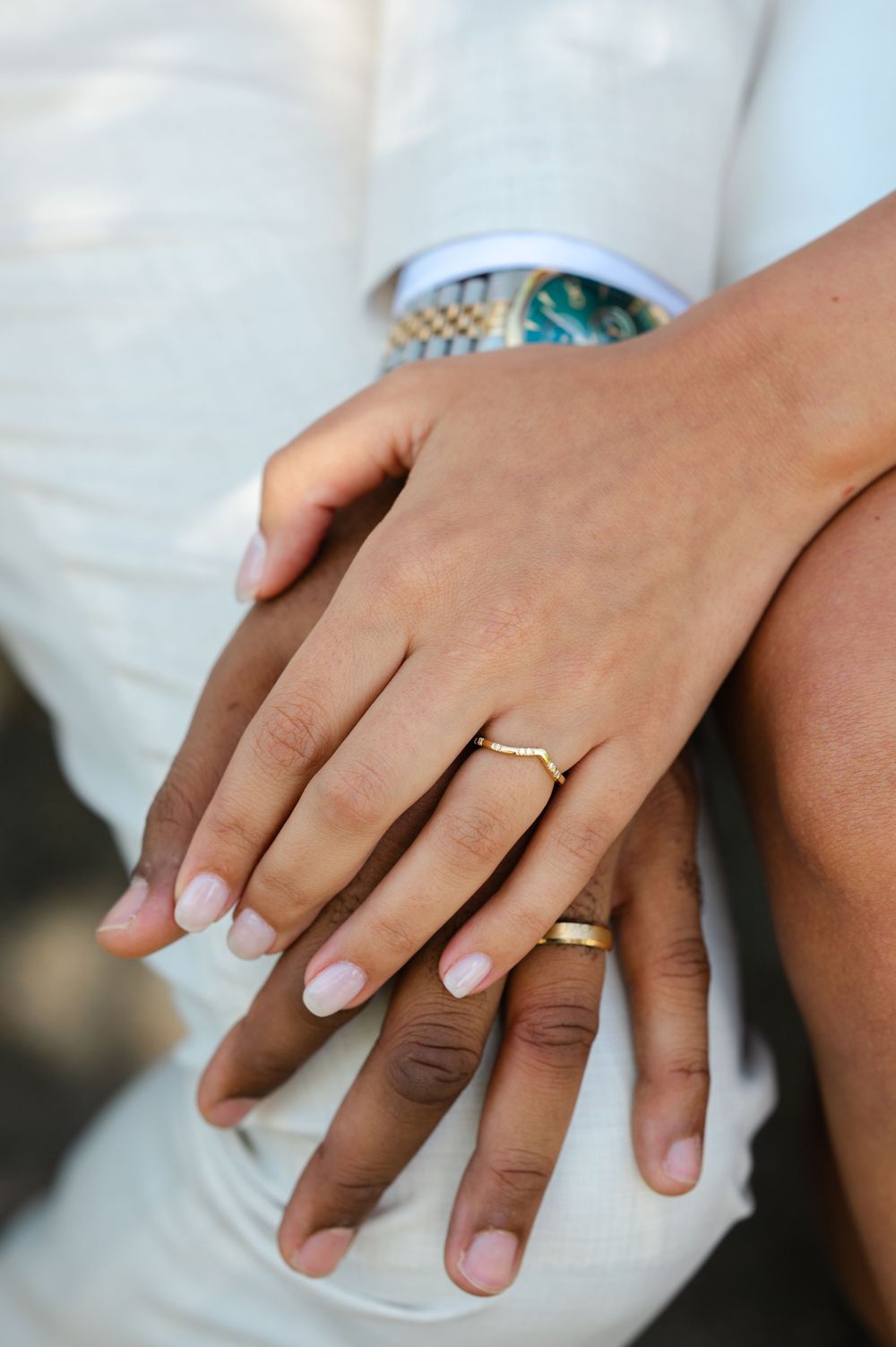 Close-up of newlyweds hands showing wedding rings and a gold watch during their wedding ceremony.