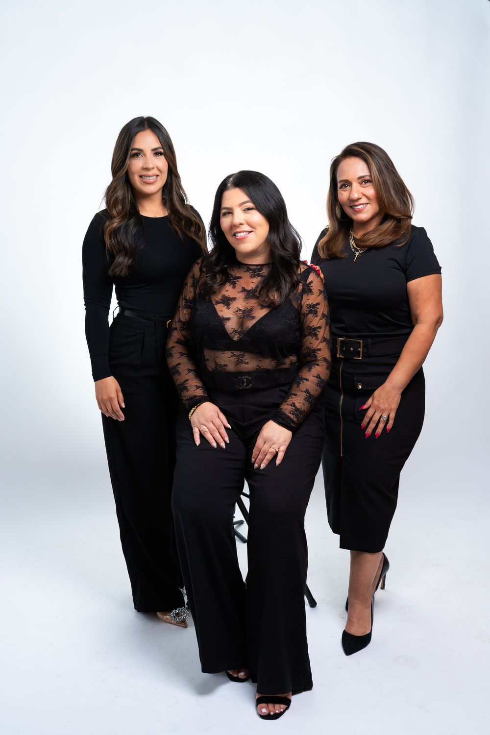 Three women in matching black outfits pose together for a professional photo against a white background.