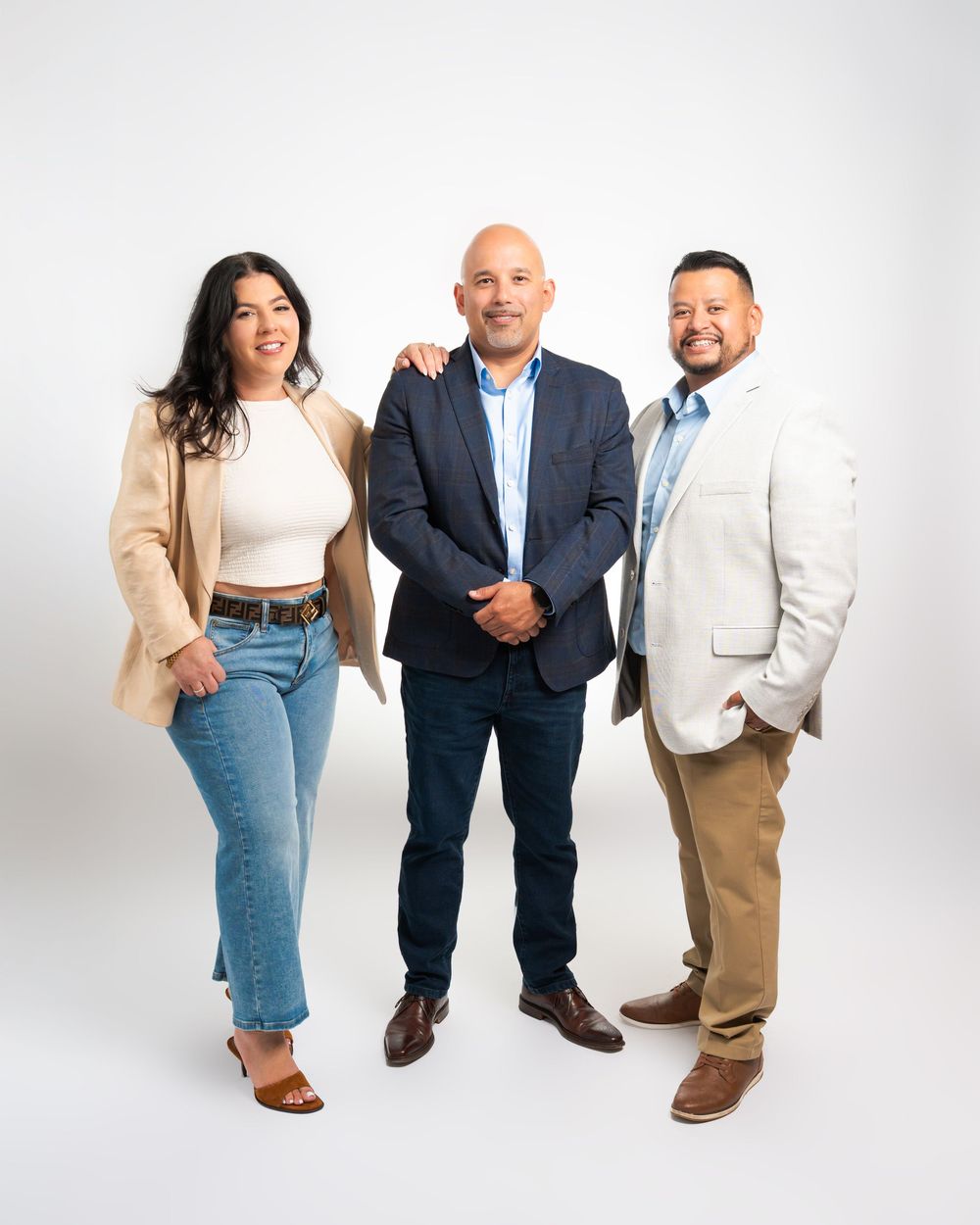 Three professionally dressed colleagues pose together smiling in a studio with a white background.