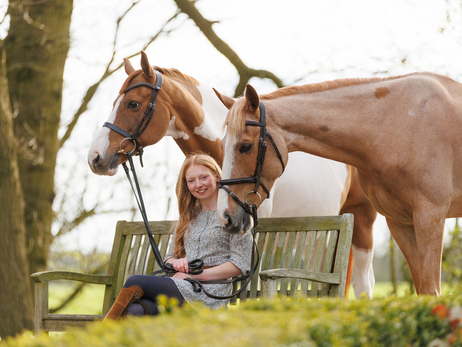 Two riders stand with their animals - a dog and a dark horse relaxing outdoors in a black and white photo.